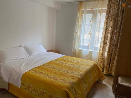 a bedroom with a bed with a yellow blanket and a window at Mountain Bloom House in Galda de Sus