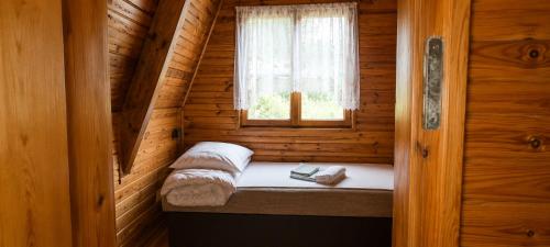 a small bed in a wooden cabin with a window at Osada Kujanki - domek wakacyjny in Zakrzewo