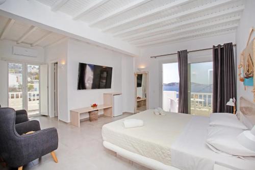 a white bedroom with a bed and a chair at Aegean View Suites Mykonos in Agios Stefanos