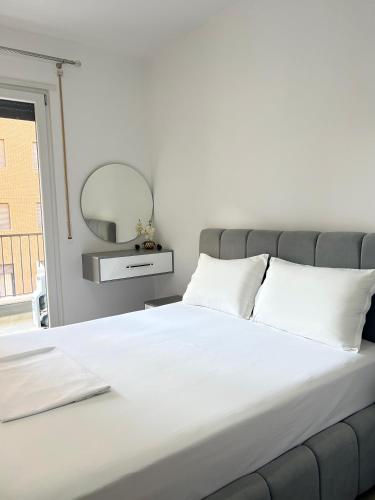 a white bed with white pillows and a mirror at Mme apartment in Kamëz