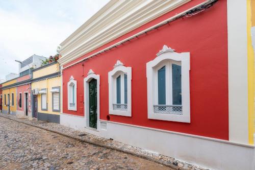 a red building with white windows on a street at Casa Butterfly in Faro