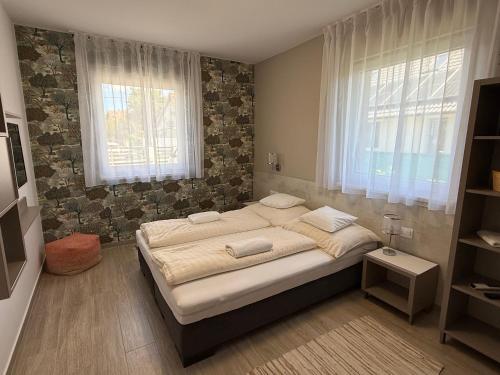 a bedroom with a bed and two windows at RoyalHill Apartman in Vonyarcvashegy