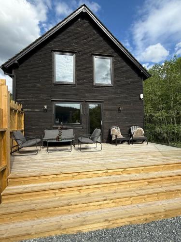 a black house with a wooden deck with chairs at By the River in Vinje