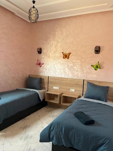 Zwei Betten in einem Zimmer mit Schmetterlingen an der Wand in der Unterkunft Dar DADA-Aglou in Tiznit