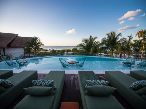 a swimming pool with chairs and the ocean in the background at Villas HM Palapas del Mar in Holbox Island