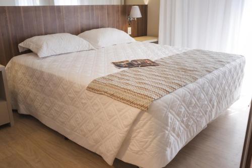 a white bed with a book on top of it at Aquarius Hotel Flat Residence in Santa Cruz do Sul