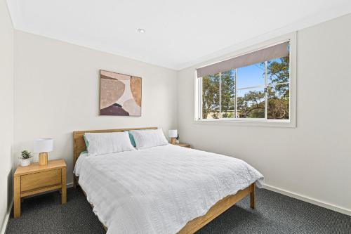 a white bedroom with a bed and a window at Mariners in the Village in Shellharbour