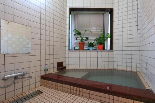 a bath tub in a tiled bathroom with a window at Ougiya Ryokan in Toyooka