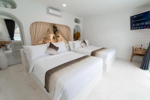 a white bedroom with two beds and a tv at Makyra by Bohemian Jogja Villas in Kejayan
