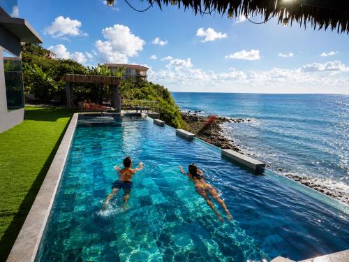 two people swimming in a swimming pool next to the ocean at condostmaarten by the sea -Adults Only- in Koolbaai