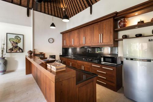 a kitchen with wooden cabinets and a stainless steel refrigerator at Villa Nesanur - Comfortable & Spacious Beachside Sanur in Sanur