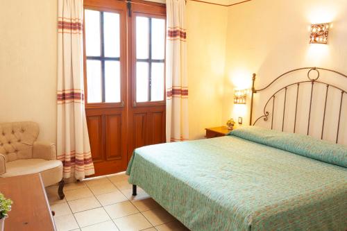 a bedroom with a bed and a chair and a window at Hotel Dainzu in Oaxaca City