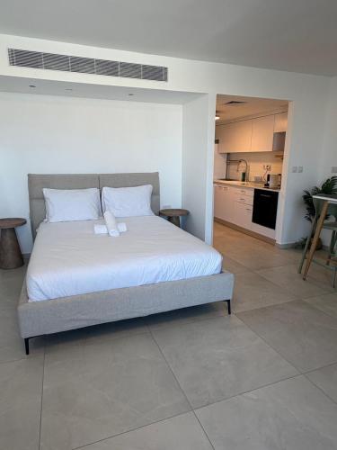 a bedroom with a bed with white sheets and a kitchen at sea&sky luxury suite מילה דירות אירוח in Eilat