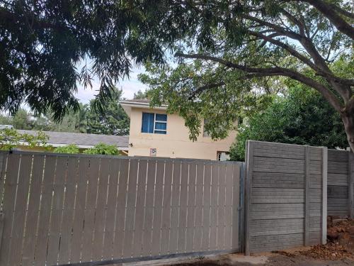 a fence in front of a house with a tree at Durbanville Place - 3 bedroom apartment in Durbanville