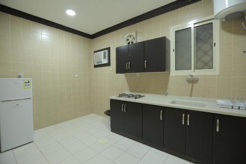 cocina con armarios negros y nevera blanca en Alrosa Furnished Apartments, en Buraidah