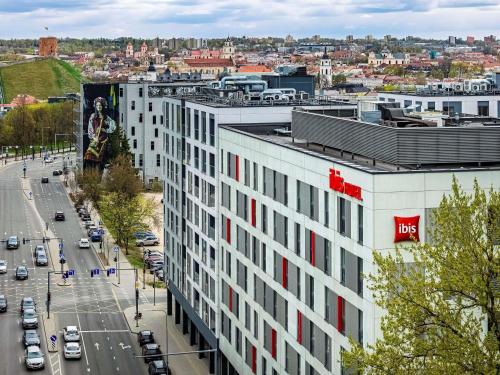 a building with a red sign on it next to a city at ibis Vilnius Centre in Vilnius