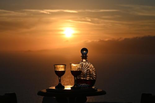 a bottle and two glasses on a table with the sunset at ⋆ 5BR Oceanside View Near Lighthouse- Pharos VM ⋆ in Mikonos