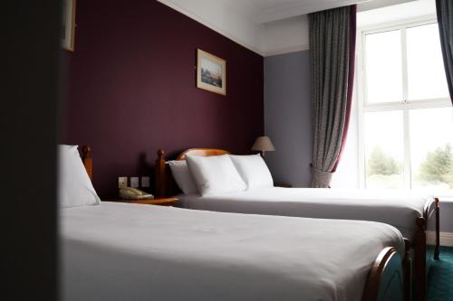 two beds in a hotel room with a window at Hydro Hotel in Lisdoonvarna