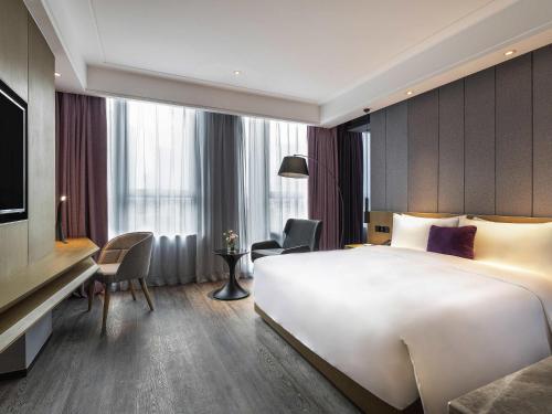 a hotel room with a large white bed and a desk at Mercure Kunshan Hi Tech Zone in Kunshan