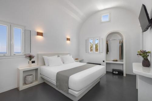 a white bedroom with a large bed and two windows at Elios Cave Suites in Oia