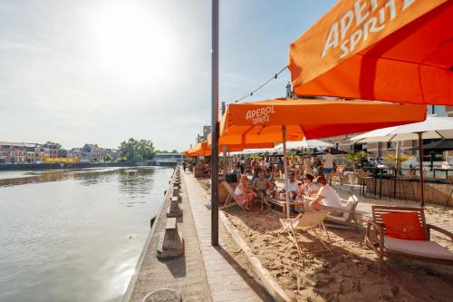 people sitting under umbrellas on a beach next to a river at Van der Valk Hotel Mechelen in Mechelen