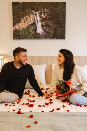 a man and a woman sitting on a bed with roses at Hotel Triveneto Gramado in Gramado