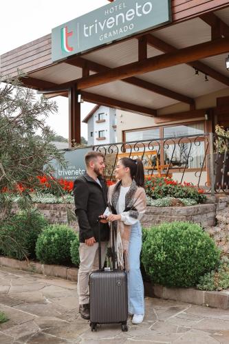 a man and woman standing next to each other with a suitcase at Hotel Triveneto Gramado in Gramado
