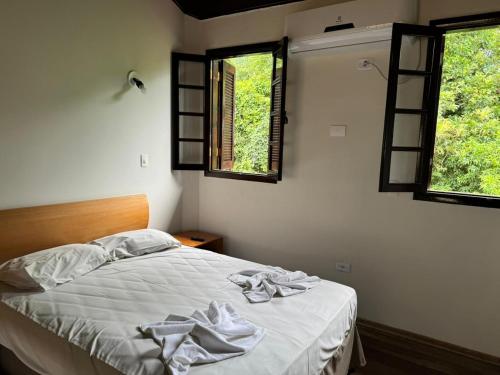 a bedroom with a bed with white sheets and two windows at Hotel da Ilha in Ilhabela