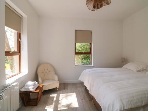 a bedroom with a bed and a chair and two windows at The Mews Suskar in Glendarragh