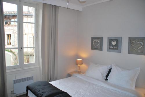 a white bedroom with a bed and a window at La Maison au Puits in Cordes-sur-Ciel
