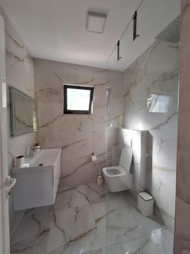 a white bathroom with a toilet and a sink at Guesthouse Deshnica in Këlcyrë