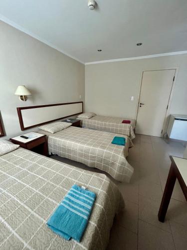 a hotel room with three beds with blue towels on them at Hotel Brasil Pindamonhangaba in Pindamonhangaba