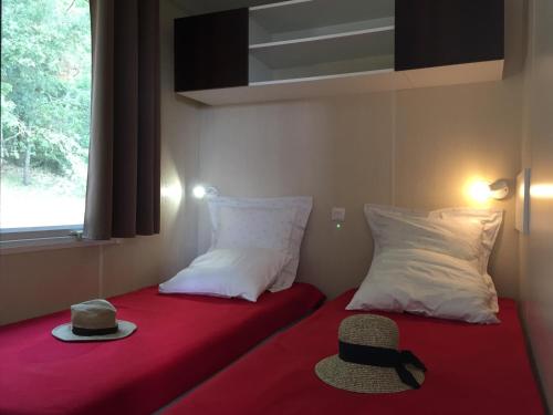 une chambre avec deux oreillers et un chapeau sur un lit rouge dans l'établissement Camping de l'Eouviere, à Montmeyan