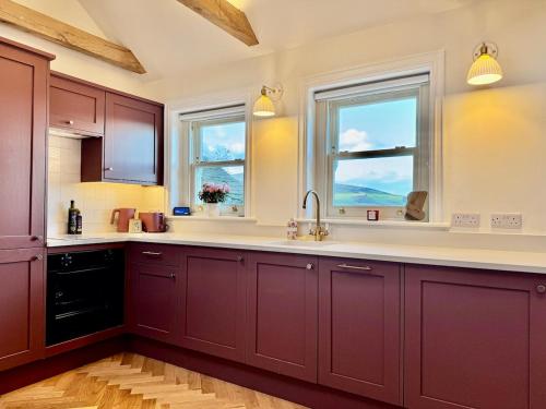 a kitchen with red cabinets and two windows at Luxury cottage for 2 in Castleton - Peak District retreat - Panoramic Views & Log burner in Castleton