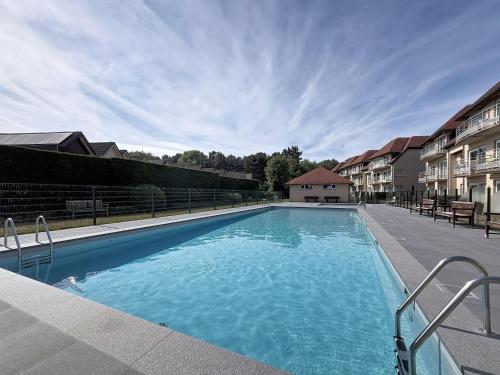 a large blue swimming pool in a yard with houses at Studio Bowie with shared pool by Interhome in De Haan