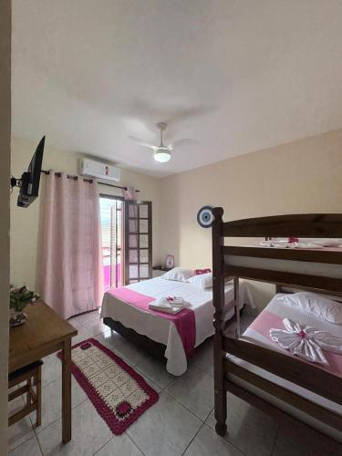 a bedroom with two beds and a table and a window at Casa Carol Vans in Peruíbe