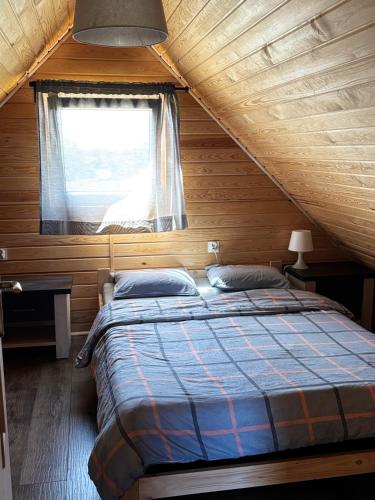 a bed in a wooden room with a window at Gawra Nad Jeziorem - całoroczne domki nad jeziorem z balią, jacuzzi i sauną, Kaszuby in Sobącz