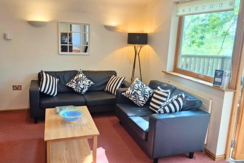 a living room with a black leather couch and a table at Scandi Style Bracken Lodge with Private Decking Sleeps 6 in Chudleigh Knighton