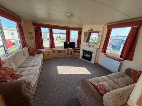 a living room with couches and a tv and windows at Bell Bank C8 - pet friendly, bed linen, close to bars and shops - Meadow Lakes Caravan & Lodge Hire in Chapel Saint Leonards