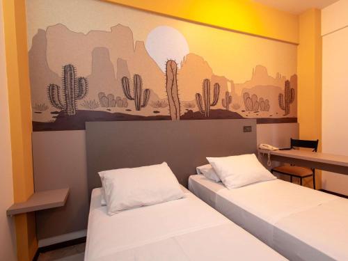 two beds in a room with a mural of cactus at ibis Styles Presidente Prudente Portal D'Oeste in Presidente Prudente