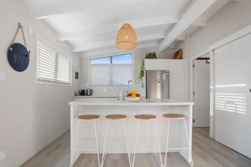 a kitchen with a white island with bar stools at Tideview Cottage - Incredible Views - Tairua in Tairua
