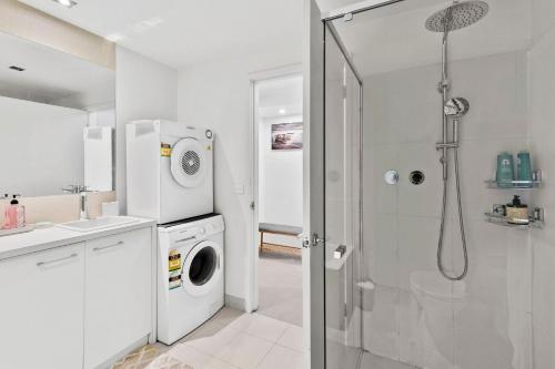 a white bathroom with a washing machine and a shower at Marley s Place in Queenscliff