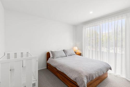 a white bedroom with a bed and a window at The Beach House in Point Lonsdale