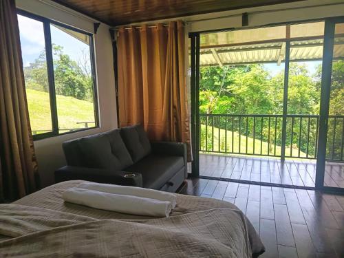 a bedroom with a bed and a couch and a balcony at INTUS Lodge Rio Celeste in El pilon
