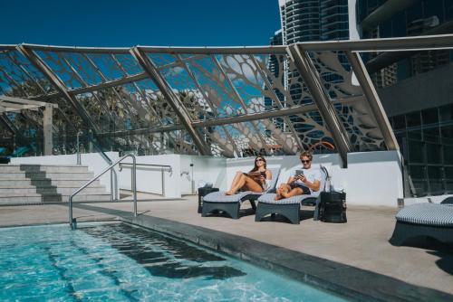 a man and woman sitting in chairs next to a swimming pool at Peppers Soul Surfers Paradise in Gold Coast