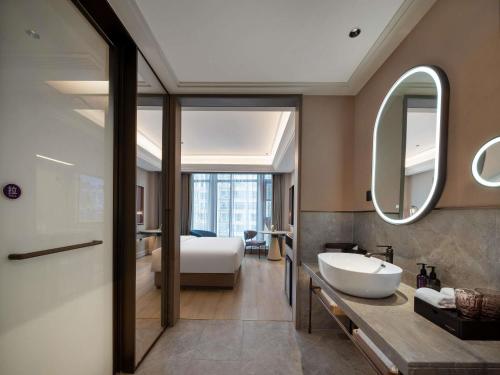 a bathroom with a sink and a bed and a mirror at Mercure Luoyang Downtown in Luoyang