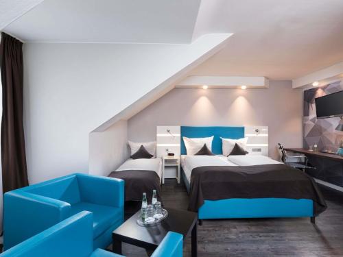a hotel room with two beds and a blue couch at ibis Styles Cologne Airport in Troisdorf