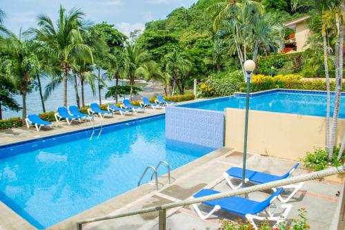 a swimming pool with blue chairs and palm trees at Bahia Pez Vela Resort in Ocotal