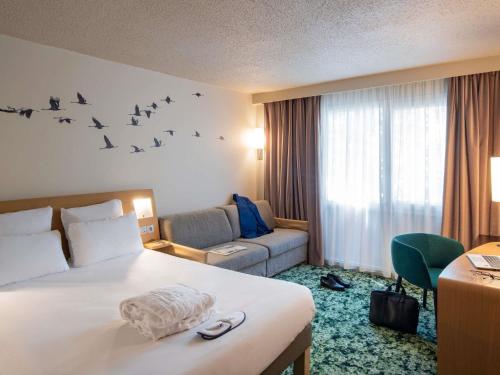 a hotel room with a bed and a couch and birds on the wall at Novotel Orléans Chemins De Sologne Demeures De Campagne in Orléans