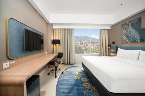 a hotel room with a bed and a desk with a tv at Mercure Bandung Nexa Supratman in Bandung